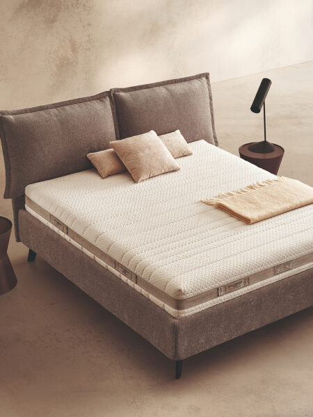 Materasso Aloe Mind Comfort posizionato su un letto in ambiente neutro con sopra cuscini e scaldapiedi warmie