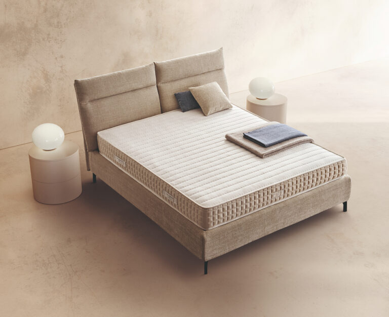 Materasso Amber posizionato su un letto in ambiente neutro con sopra cuscini e scaldapiedi warmie