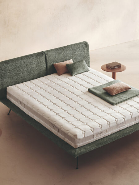 Materasso Cashmere Comfort posizionato su un letto in ambiente neutro con sopra cuscini e scaldapiedi warmie