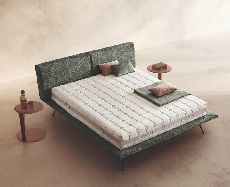 Materasso Cashmere Comfort posizionato su un letto in ambiente neutro con sopra cuscini e scaldapiedi warmie