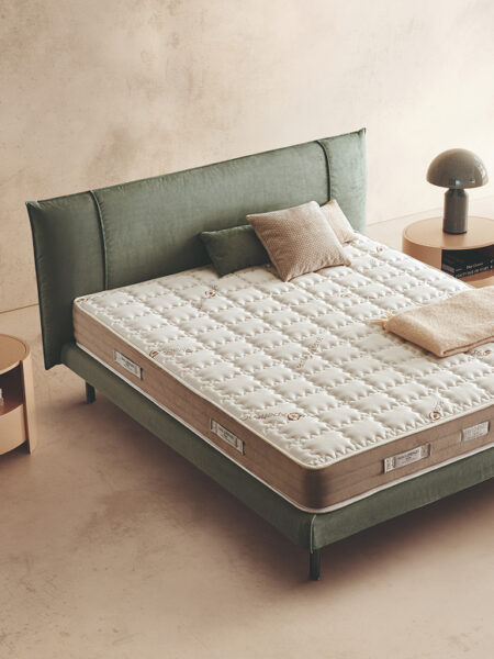 Materasso Harmony Fresh posizionato su un letto in ambiente neutro con sopra cuscini e scaldapiedi warmie