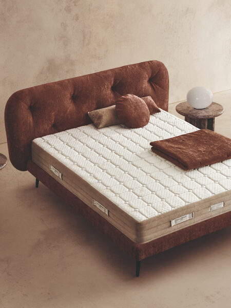 Materasso Idra Fresh posizionato su un letto in ambiente neutro con sopra cuscini e scaldapiedi warmie