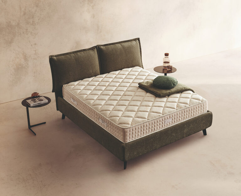 Materasso Incanto Memory posizionato su un letto in ambiente neutro con sopra cuscini e scaldapiedi warmie