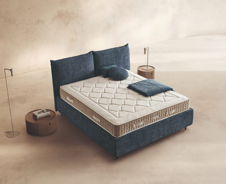 Materasso Luxor Mind posizionato su un letto in ambiente neutro con sopra cuscini e scaldapiedi warmie
