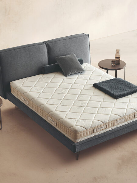 Materasso Memory First posizionato su un letto in ambiente neutro con sopra cuscini e scaldapiedi warmie