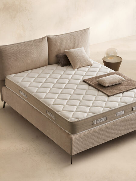 Materasso Memory Sleep posizionato su un letto in ambiente neutro con sopra cuscini e scaldapiedi warmie