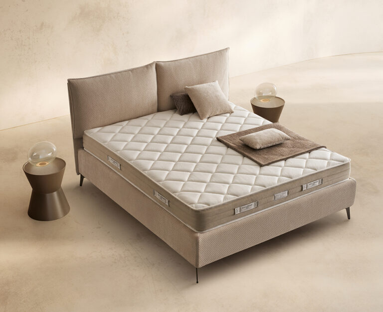 Materasso Memory Sleep posizionato su un letto in ambiente neutro con sopra cuscini e scaldapiedi warmie