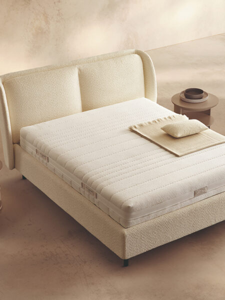 Materasso Memory Touch Evolution posizionato su un letto in ambiente neutro con sopra cuscini e scaldapiedi warmie