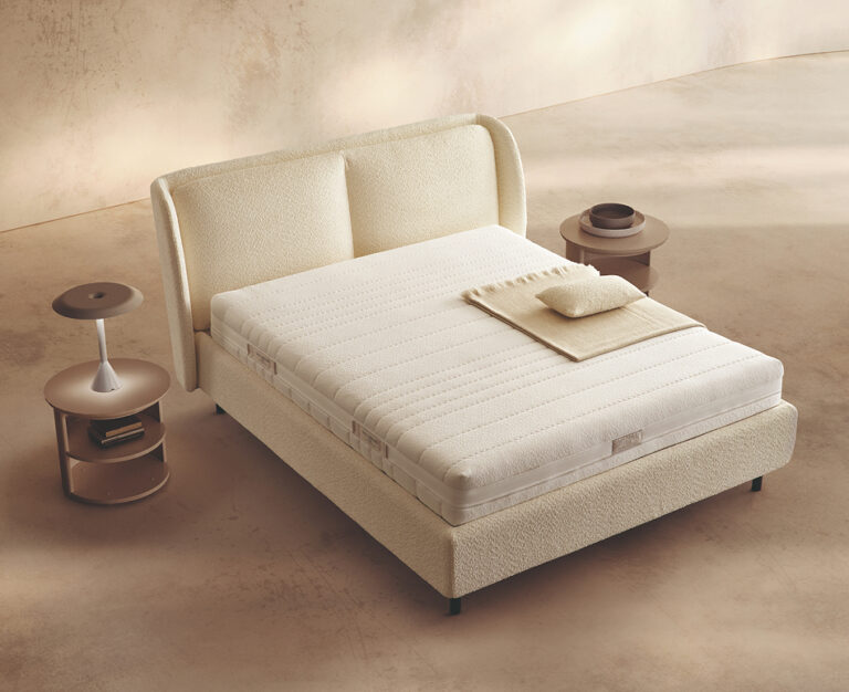 Materasso Memory Touch Evolution posizionato su un letto in ambiente neutro con sopra cuscini e scaldapiedi warmie