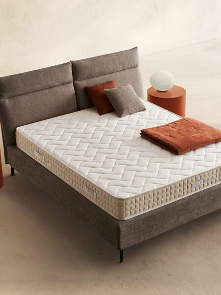 Materasso Noor posizionato su un letto in ambiente neutro con sopra cuscini e scaldapiedi warmie