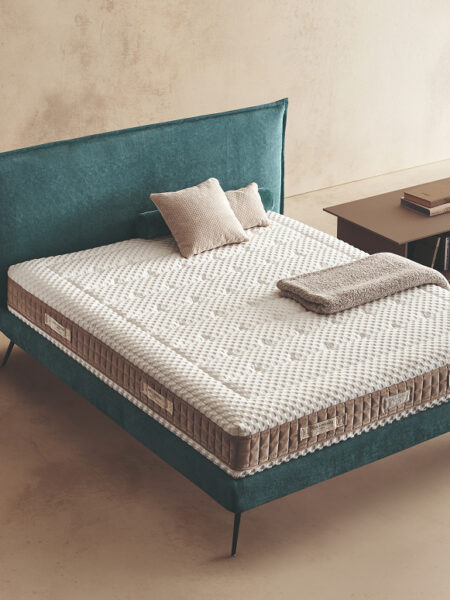 Materasso Orthoease posizionato su un letto in ambiente neutro con sopra cuscini e scaldapiedi warmie