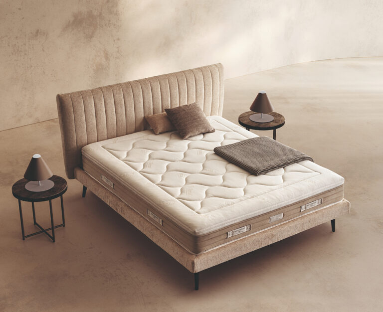 Materasso Platinum Fresh posizionato su un letto in ambiente neutro con sopra cuscini e scaldapiedi warmie