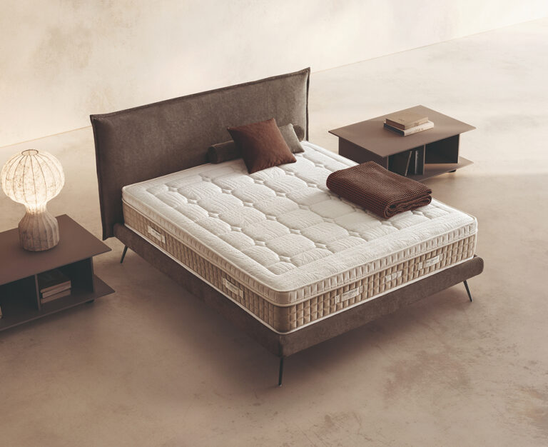 Materasso Pocket Foam posizionato su un letto in ambiente neutro con sopra cuscini e scaldapiedi warmie