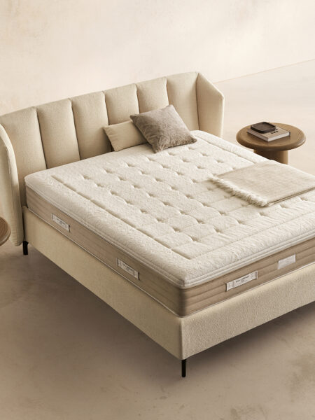 Materasso Prestige Memory posizionato su un letto in ambiente neutro con sopra cuscini e scaldapiedi warmie