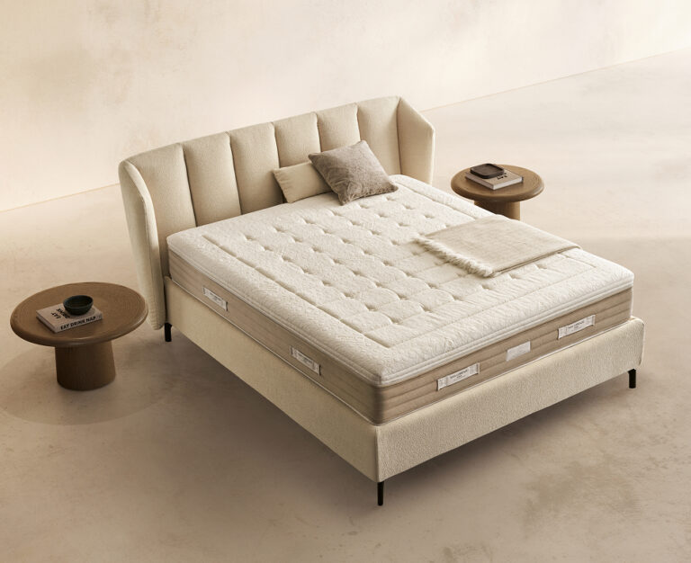 Materasso Prestige Memory posizionato su un letto in ambiente neutro con sopra cuscini e scaldapiedi warmie