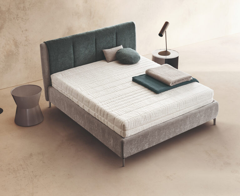 Materasso Pretty Latex posizionato su un letto in ambiente neutro con sopra cuscini e scaldapiedi warmie