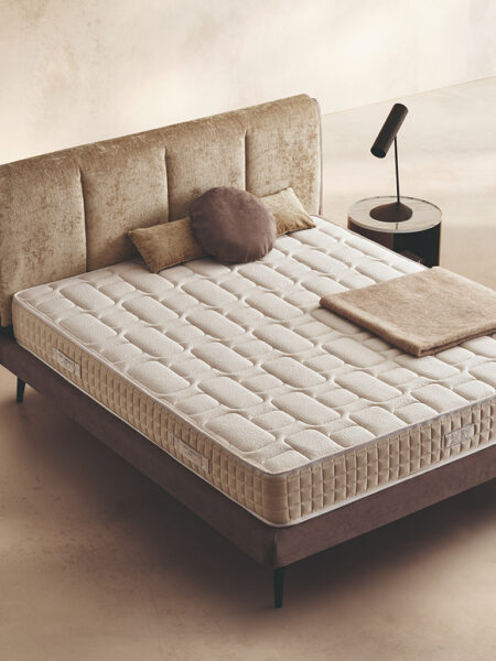 Materasso Regard posizionato su un letto in ambiente neutro con sopra cuscini e scaldapiedi warmie