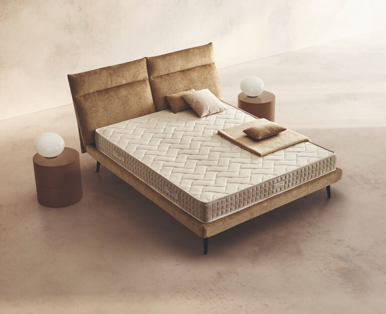 Materasso Relax posizionato su un letto in ambiente neutro con sopra cuscini e scaldapiedi warmie