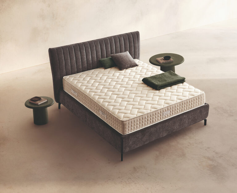 Materasso Relax Plus Mind posizionato su un letto in ambiente neutro con sopra cuscini e scaldapiedi warmie