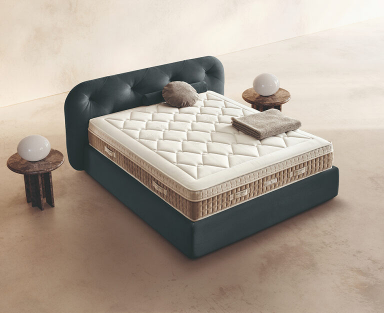 Materasso Relax Rest posizionato su un letto in ambiente neutro con sopra cuscini e scaldapiedi warmie