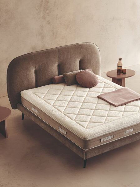 Materasso Royal Fresh posizionato su un letto in ambiente neutro con sopra cuscini e scaldapiedi warmie