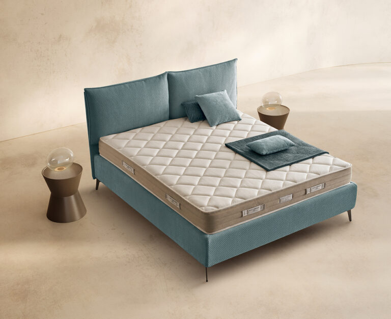 Materasso Sleep Fresh posizionato su un letto in ambiente neutro con sopra cuscini e scaldapiedi warmie