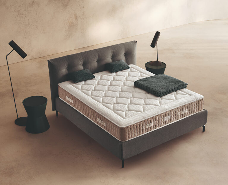 Materasso Zeus Fresh Zip posizionato su un letto in ambiente neutro con sopra cuscini e scaldapiedi warmie